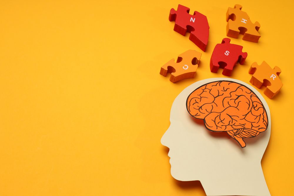 Paper cut out of head with brain & puzzle pieces on orange background, copy space