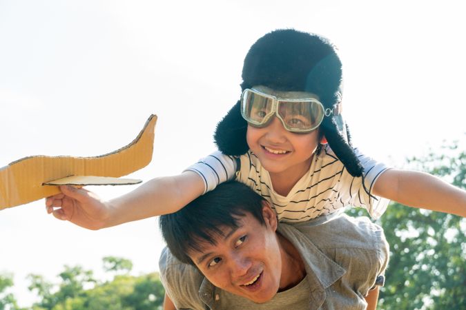 Father giving son piggy back while he’s playing with toy plane in  park