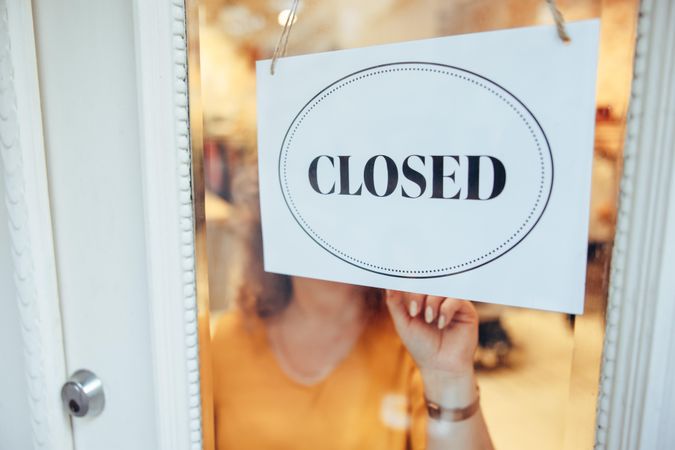 Female owner putting closed sign on her clothing store front door