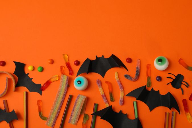 Concept of halloween with bats and candies on orange background