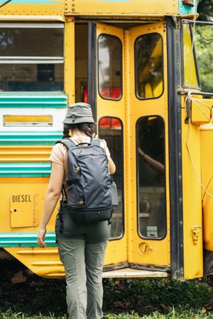 Woman with backpack entering a yellow bus