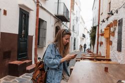 Young woman with denim jacket and backpack with phone outside at counter