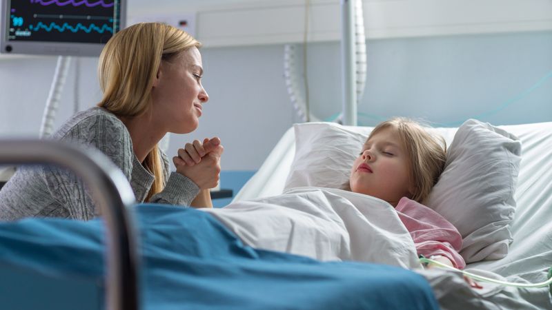 Cute Little Girl Sleeps on the Bed in the Children's Hospital, Her Mother Sits Beside, Worrying but Hopeful
