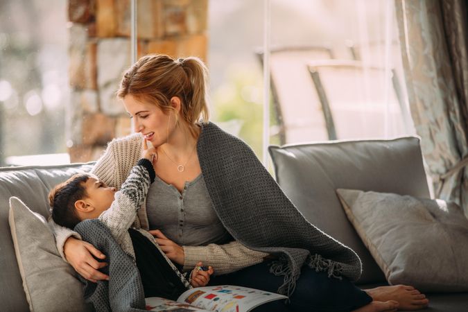 Little boy touching mouth of his mother sitting in living room