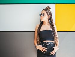 Charming teenage girl with dreadlocks in sunglasses nearby colorful wall