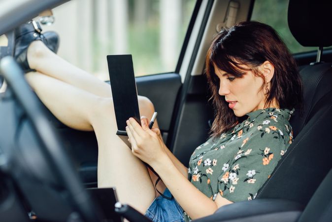 Female wearing flowered shirt and shorts writing notes while sitting in parked car