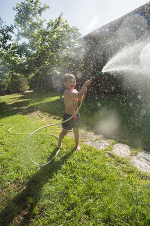 Little child having fun with garden hose and water