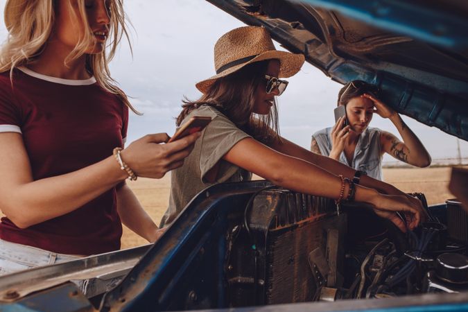 Woman trying to fix the car with friends making phone calls for help
