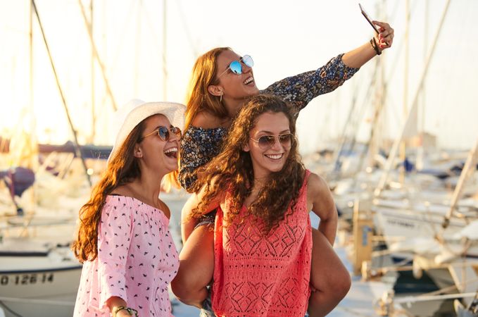 Woman carrying girlfriend on back and taking selfie