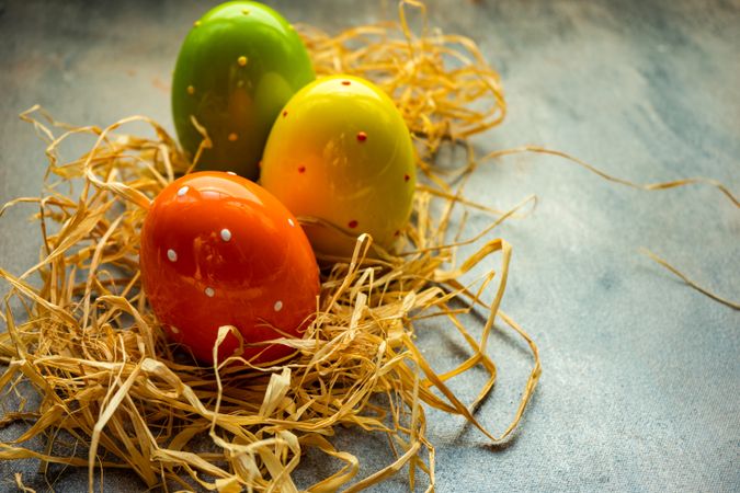 Decorative spotted Easter eggs in straw on grey table