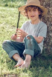 Cheerful boy in wicker hat and with stick under tree