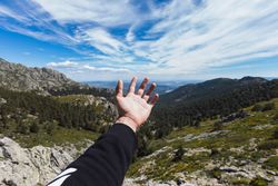 Person stretching hand to blue sky above mountain valley
