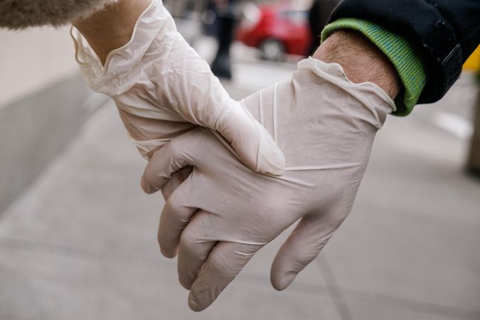 Two people wearing plastic gloves holding hands