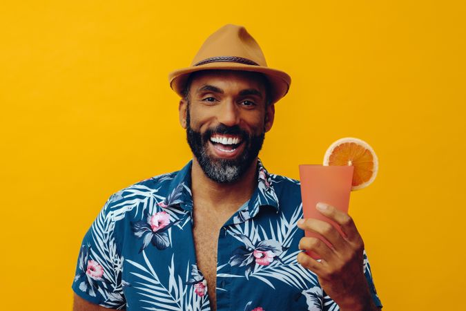 Male smiling happily with a cocktail while wearing colorful shirt with yellow background