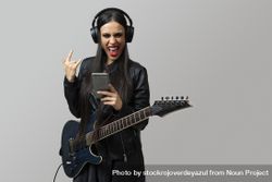A young woman, guitarist, enjoys listening to music with the wireless headphones while make horns symbol with her hand 4Baal3