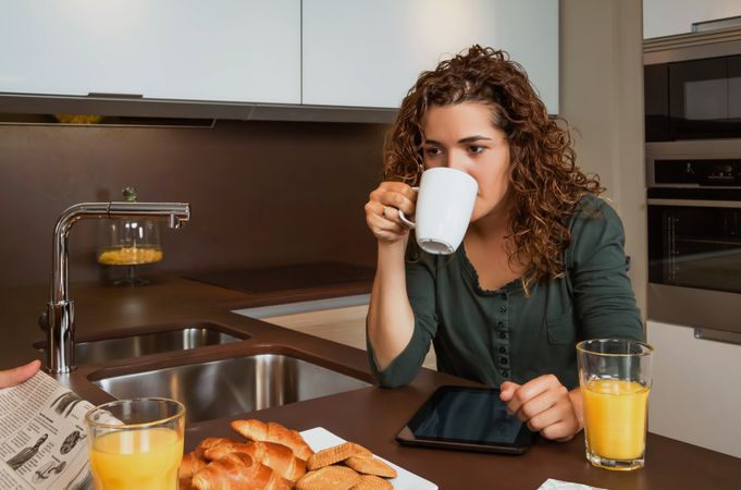 Woman sipping coffee over tablet screen at breakfast