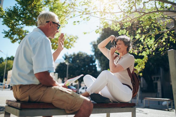 Older couple sitting outdoors in the city taking photos of each other on vacation