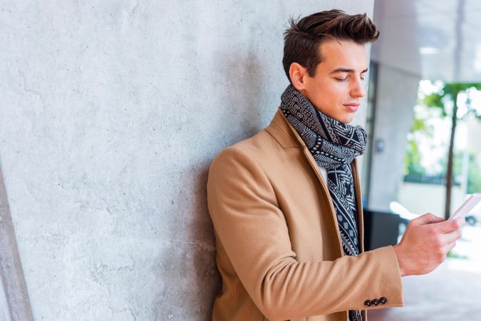 Man in camel coat and scarf looking at phone outside