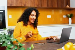 Woman in colorful kitchen speaking on a video call on her laptop