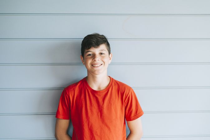 Portrait of a cheerful male teen leaning on wood wall while looking at camera