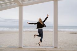 Joyful woman jumping raising hands up on wooden beach pier