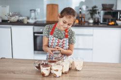 tiramisu making process in the kitchen- little girl making Italian desert with cocoa and espresso-dipped ladyfingers with mascarpone cream
