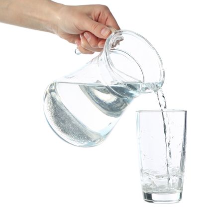 Hand pouring water in glass from pitcher in plain studio