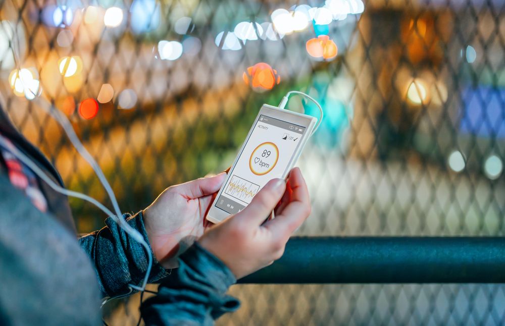 Close up of unrecognizable female athlete holding cellphone with heart rate monitor at night
