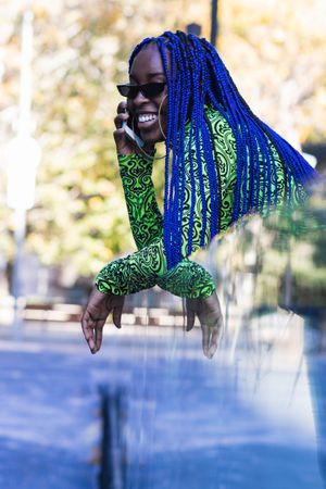 Cheerful Black woman with blue hair speaking on smartphone