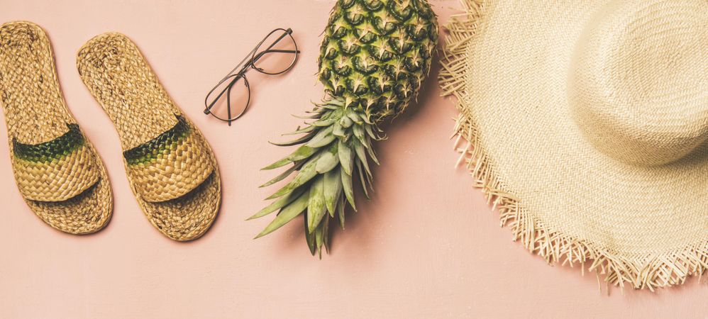Sandals, glasses, pineapple, straw hat on pink background, wide composition