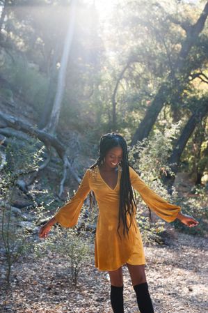 Young Black woman in velvet dress swinging her arms with the sun behind her