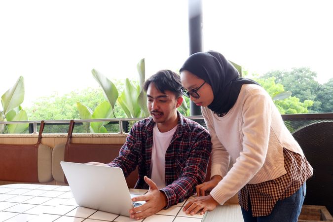 Two Young Asian Working People, Discussing at the Cafe Table, Working with Laptop Explaining File on Screen
