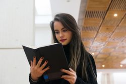 Woman standing along bookshelves and holding open book