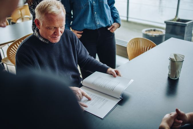 Mature businessman sitting at table and reading a contract document for team