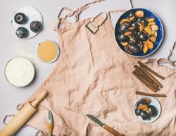 Baking ingredients and tools, plums, pastry brush, cinnamon, eggs on pink apron