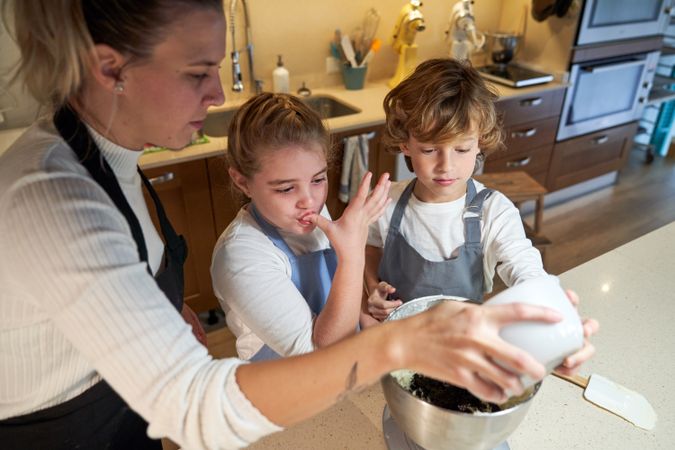 Two boys and a girl with apron in the kitchen mixing ingredients preparing cupcakes