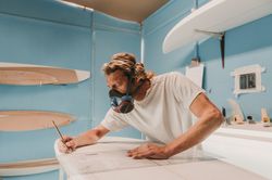 Man in respirator measuring surf board in workshop