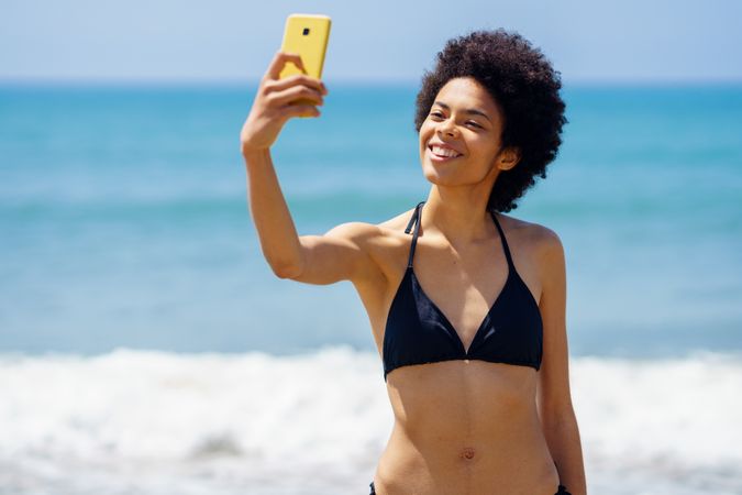 Joyful woman in biking standing near the ocean taking a selfie