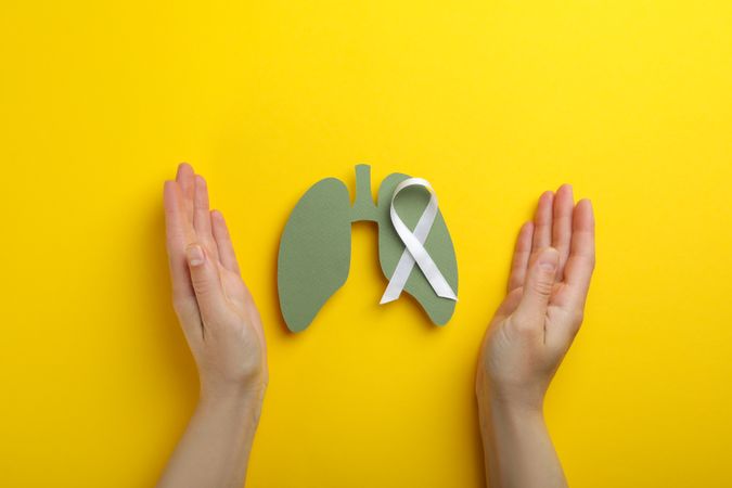 Lungs cut out of green paper with ribbon surrounded by hands