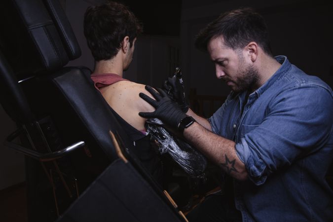 Master doing tattoo on forearm of male customer