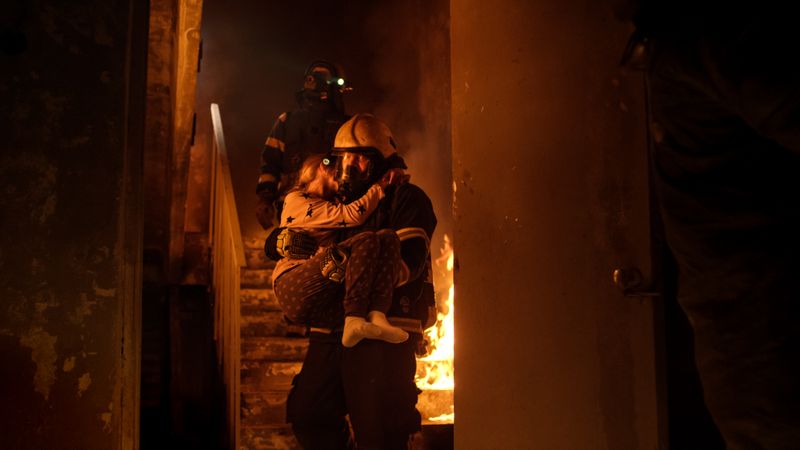 Brave fireman descends stairs of a burning building with a saved girl in his arms.