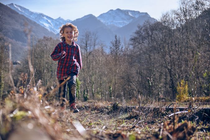 Cheerful boy running on dry grass in mountainous valley
