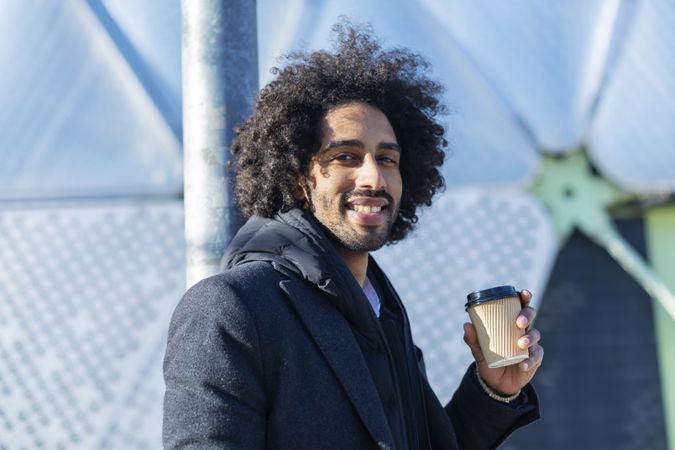 Happy Black man in jacket with warm beverage standing outside