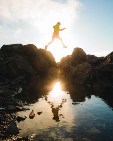 Man jumping on rocks with reflection on water