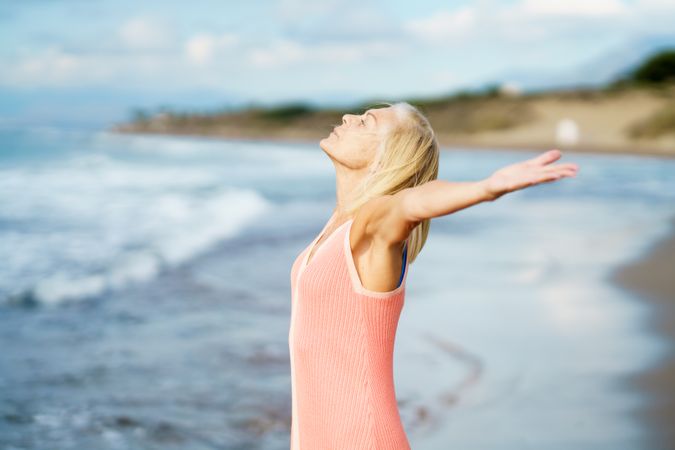 Sideview of carefree woman standing on the coast with her arms outstretched