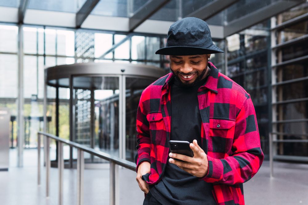 Cheerful Black male with smartphone in contemporary building
