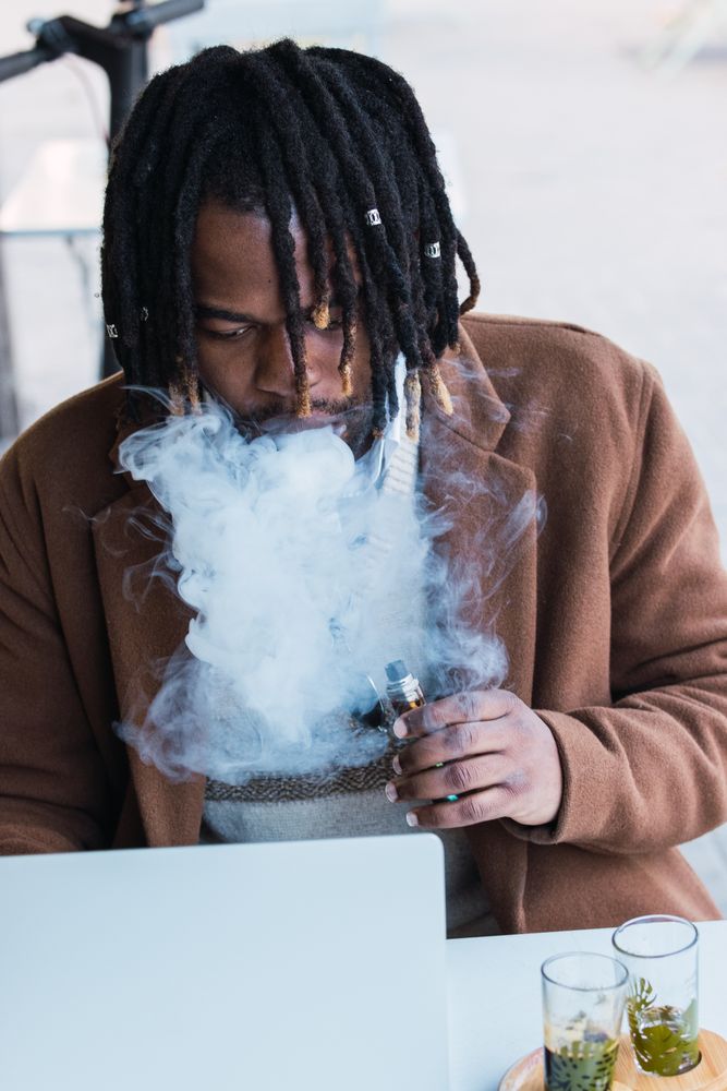 Smoking Black man using laptop on restaurant terrace