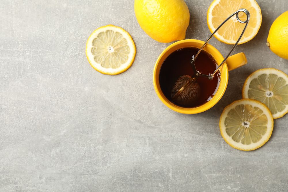 Cup of tea and lemons on grey background, space for text