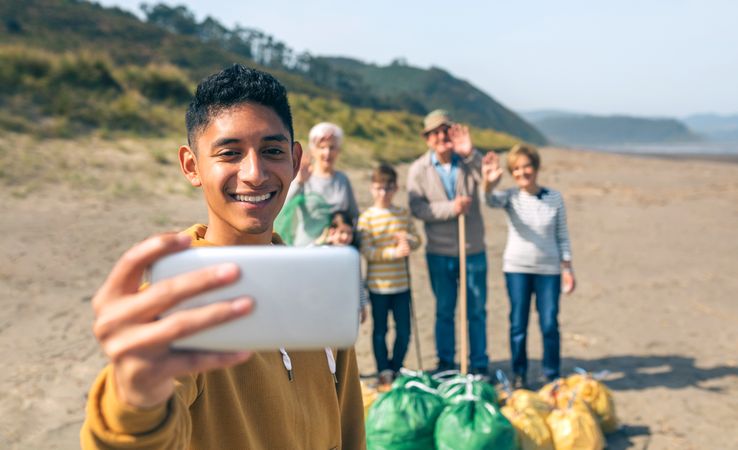 Young man taking selfie to group of volunteers after cleaning beach
