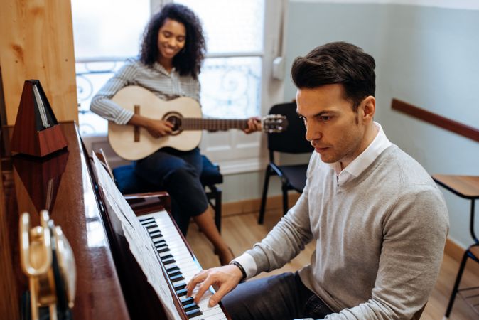 Man playing piano near woman playing guitar in studio